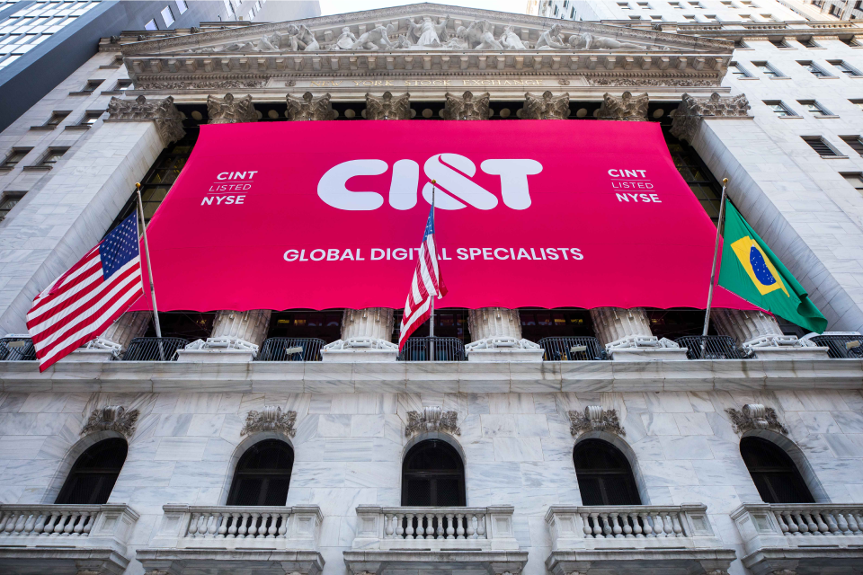 A huge CI&T banner tied to the front columns of a classic-sytle building, and there are USA and Brazil flags in front of it