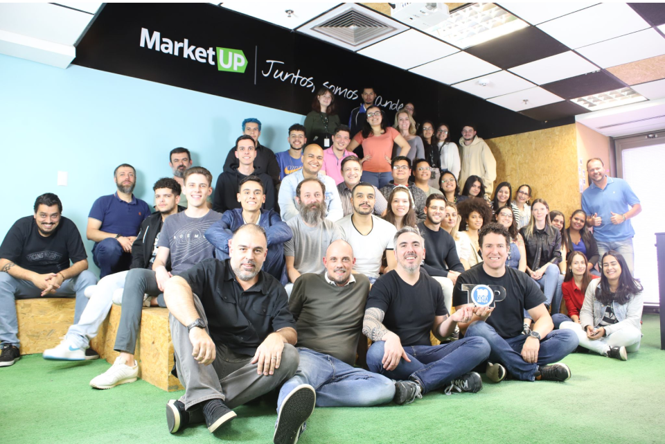 A group of mre than 40 people, gathered on a long bench, smiling, some are sitting and some are standing up