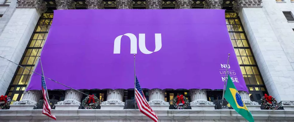 A huge Nubank banner tied to the front columns of a classic-sytle building, and there are USA and Brazil flags in front of it