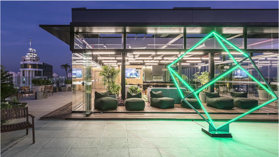 A huge luminous green cube-like monument in front of a modern building at night 