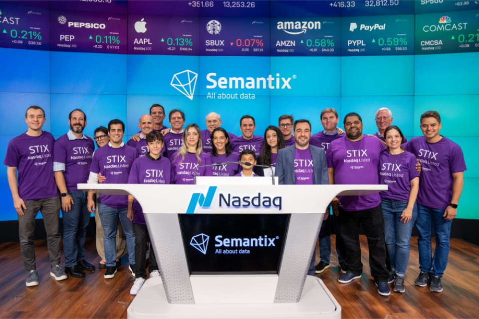 A group of 21 people wearing the same purple shirt gathered behing a white desk, smiling to the camera